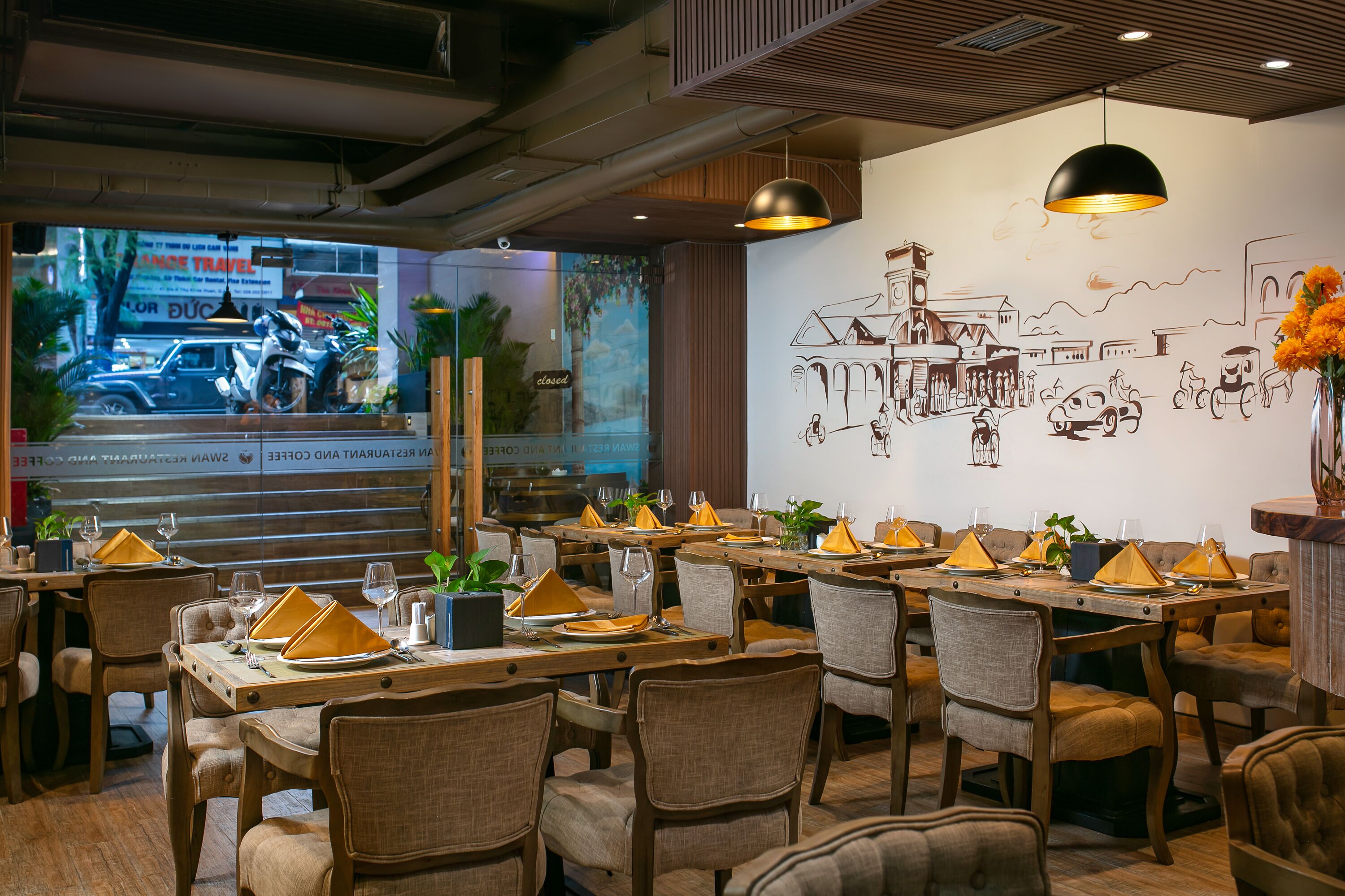 Un restaurante con mesas y sillas de madera, un mural en la pared y vista a la calle.