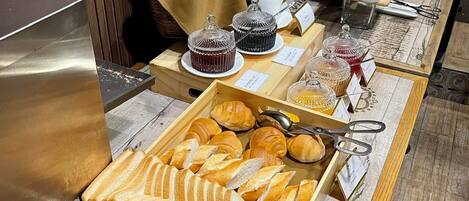 A buffet with various breads, pastries, and condiments.