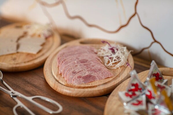 A wooden cutting board with sliced meat and shredded vegetables.
