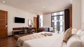 Quarto de hotel com uma cama, uma escrivaninha com computador, televisão e varanda com vista.
