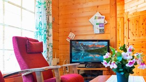 Een gezellig interieur van een chalet met houten afwerking, een televisie aan de muur, een rode stoel, een tafel met een bloevas en een raam met gordijnen.