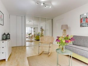 Un salon moderne avec un canapé, un fauteuil, une petite table ornée de fleurs, une lampe et un tableau accroché au mur.