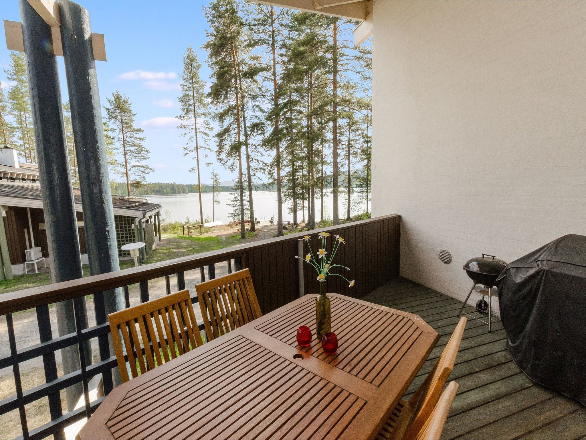 Eine Holzterrasse mit Tisch, Stühlen, einem Blumenvasen und einem Grill.