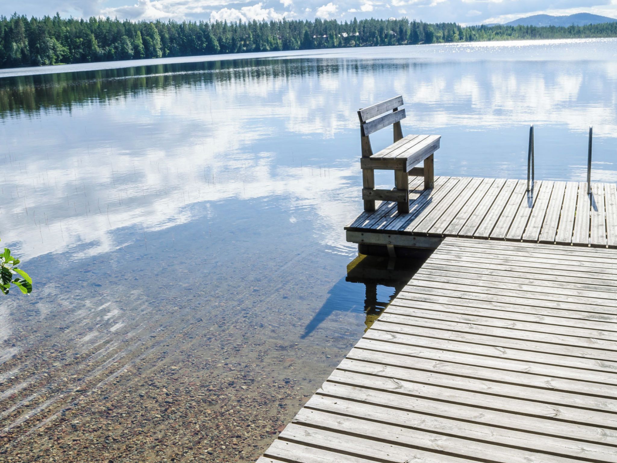 Eine Holzstege führt in einen ruhigen See, auf dem eine Bank steht.