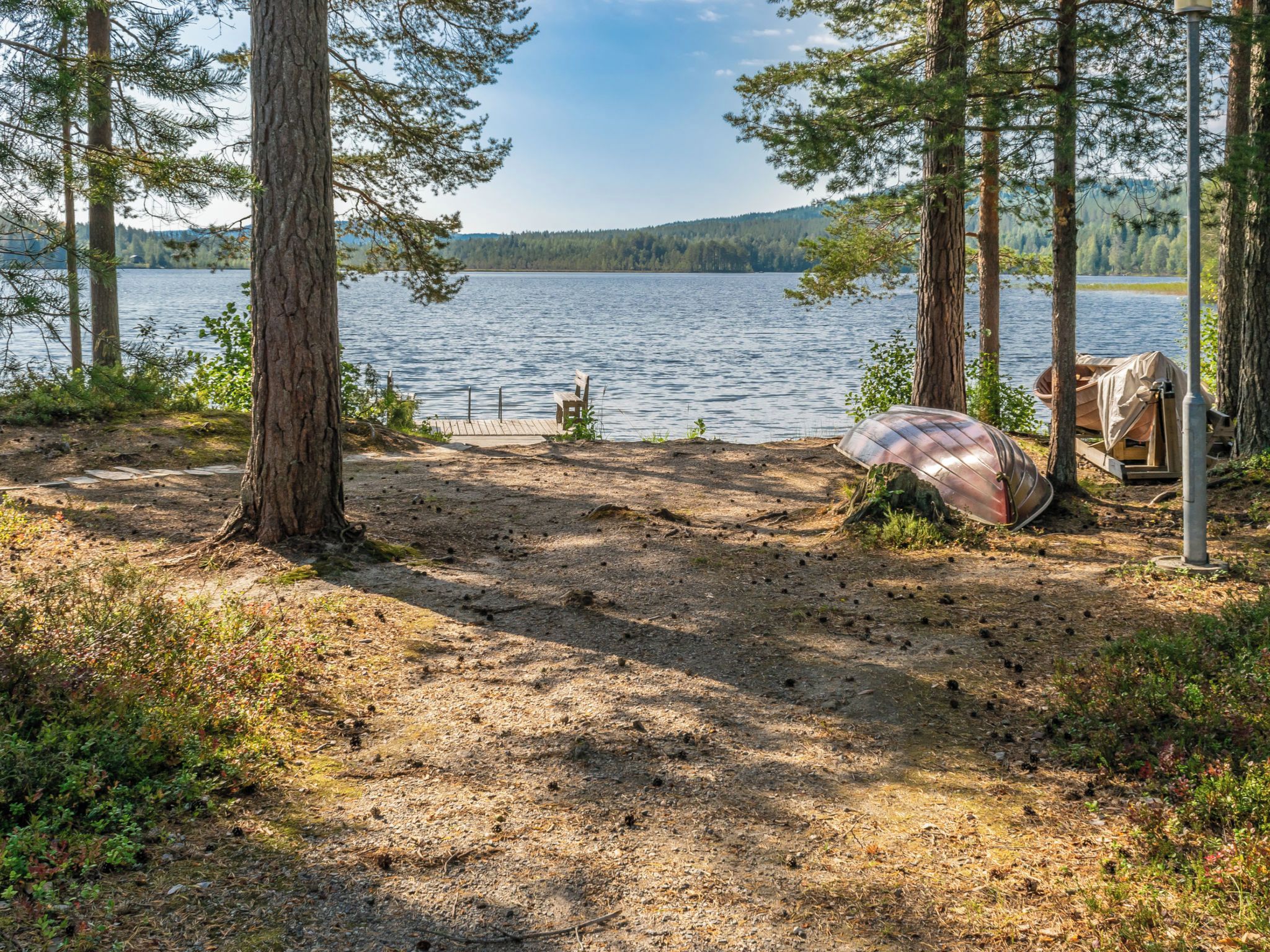 Un terrain de camping au bord du lac, doté d’une terrasse en bois, d’un canoë abrité et d’une chaise.