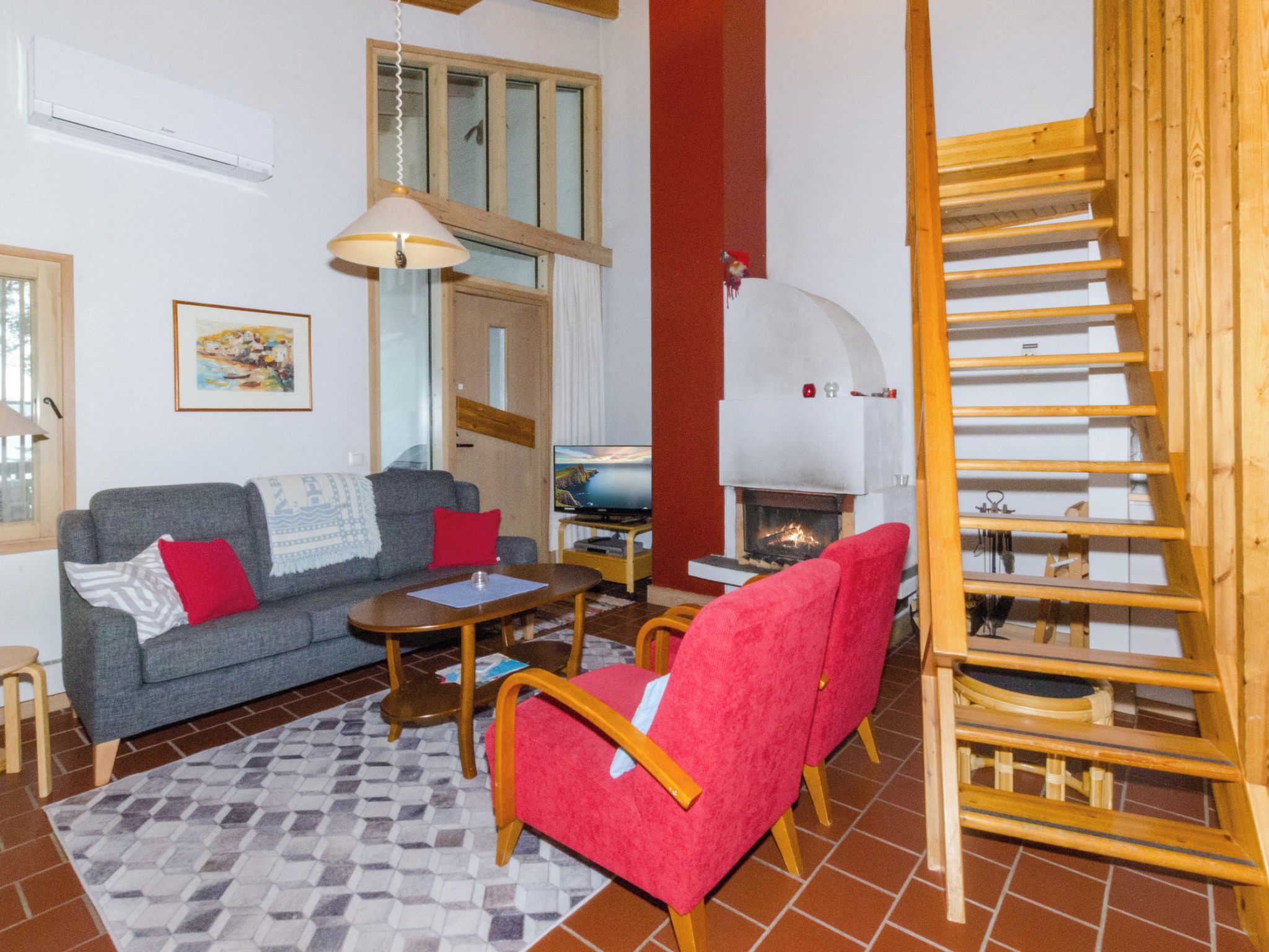 A living room with a sofa, armchair, coffee table, fireplace, and a wooden staircase.
