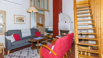 A living room with a sofa, armchair, coffee table, fireplace, and a wooden staircase.