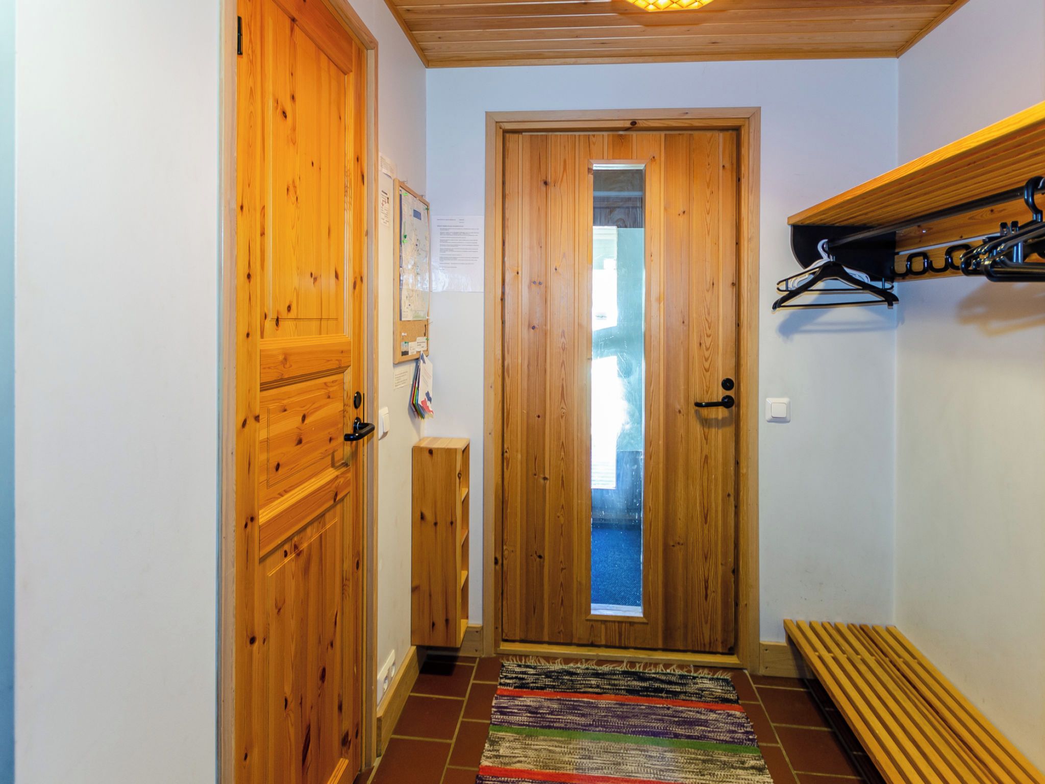 A hallway with wooden doors, a bench, and a hanging coat rack.