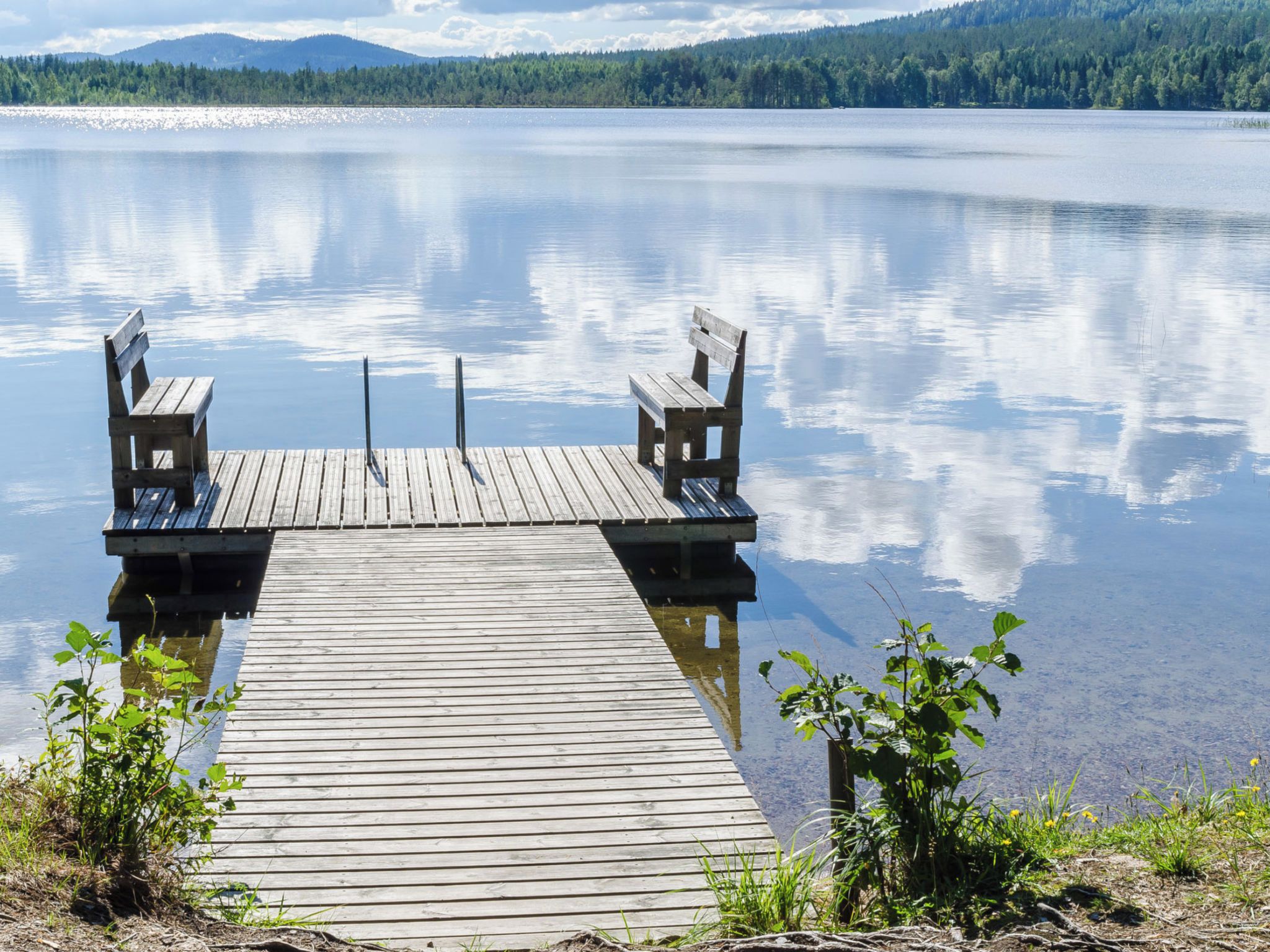 A wooden dock extending into calm water with two benches on either end.