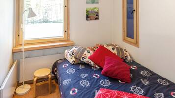 A bedroom with a bed, a small stool, a desk, and a window.