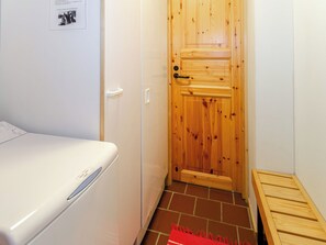 En smal hall med en trädörr, en vit apparat på vänster sida och en röd matta på golvet.