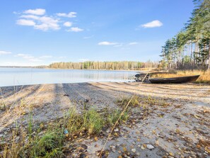 Une plage au bord d’un lac, avec un bateau, un ciel dégagé et une forêt en arrière-plan.