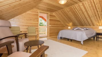 A cozy, wooden interior with a bed, two chairs, a small table, and a view of the outdoors.