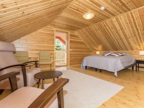 A cozy, wooden interior with a bed, two chairs, a small table, and a view of the outdoors.