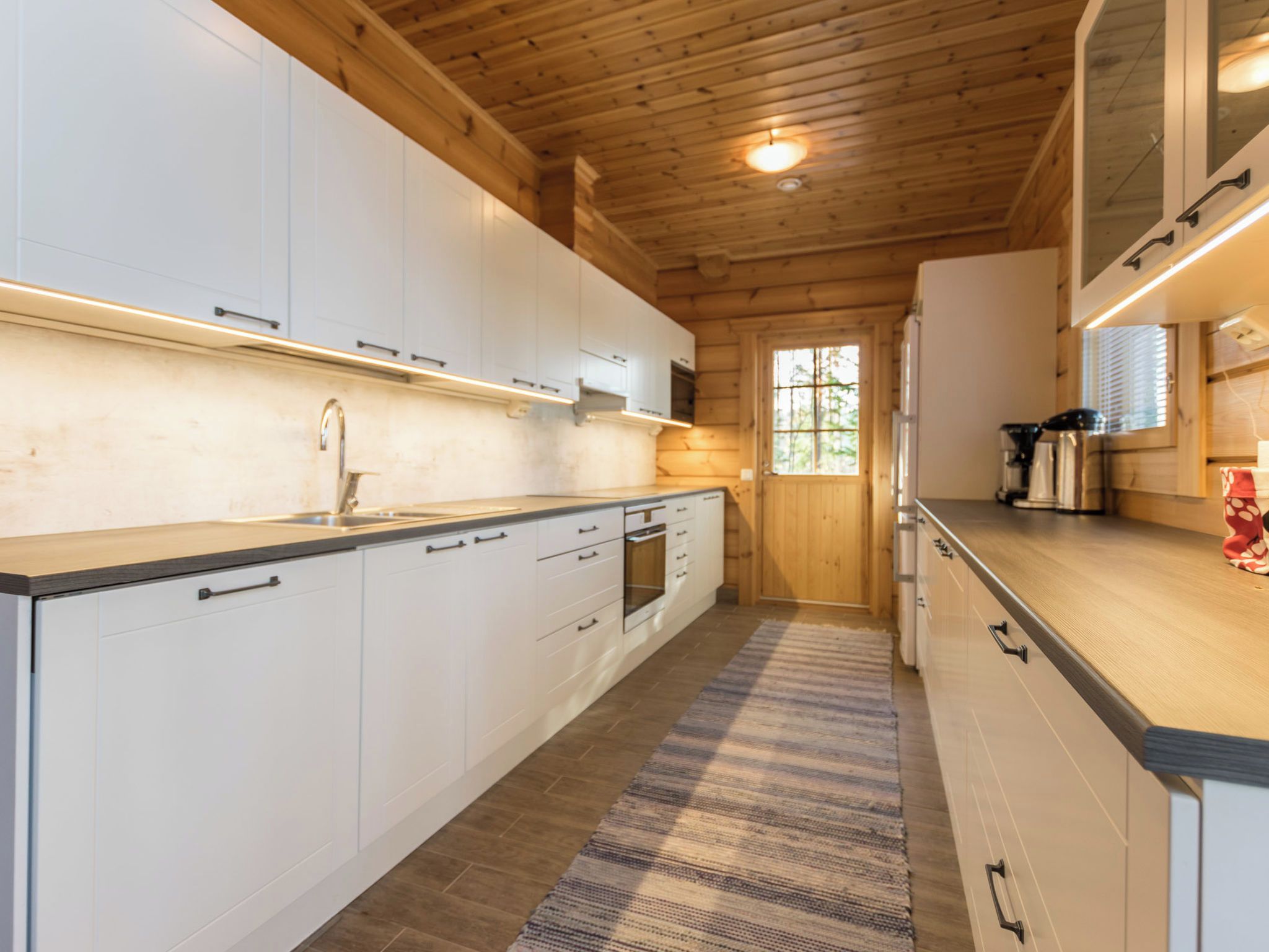 Una cocina moderna con armarios blancos, un lavamanos de acero inoxidable y un techo de madera.