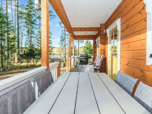 Een houten terras met een tafel, stoelen, een barbecue en uitzicht op een bos en een meer.