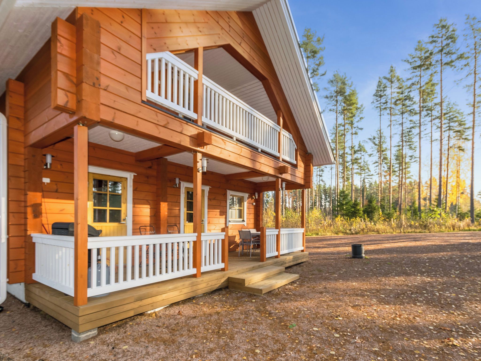 Een houten vakantiehuis met twee verdiepingen, een balkon en een overdekte veranda, met uitzicht op een bos.