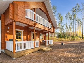 Een houten vakantiehuis met twee verdiepingen, een balkon en een overdekte veranda, met uitzicht op een bos.
