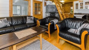 Una sala de estar acogedora con chimenea, techo de madera y una cocina visible a través de un umbral abierto.