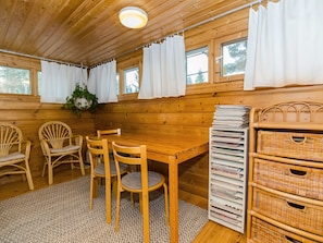 A wooden interior with a dining table, chairs, a hanging plant, and wicker storage.