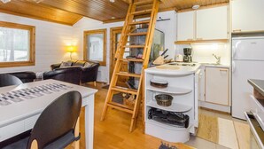 Interior acogedor de una cabaña con comedor, cocina y una escalera de madera que sube a un altillo.