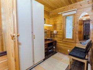 A wooden cabin interior with a wardrobe, desk, chair, and a window with blinds.