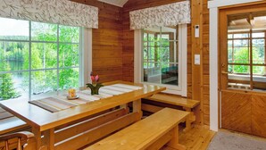 Eine Holzhütte mit Esstisch und Bänken, großen Fenstern mit Vorhängen und einer Tür.