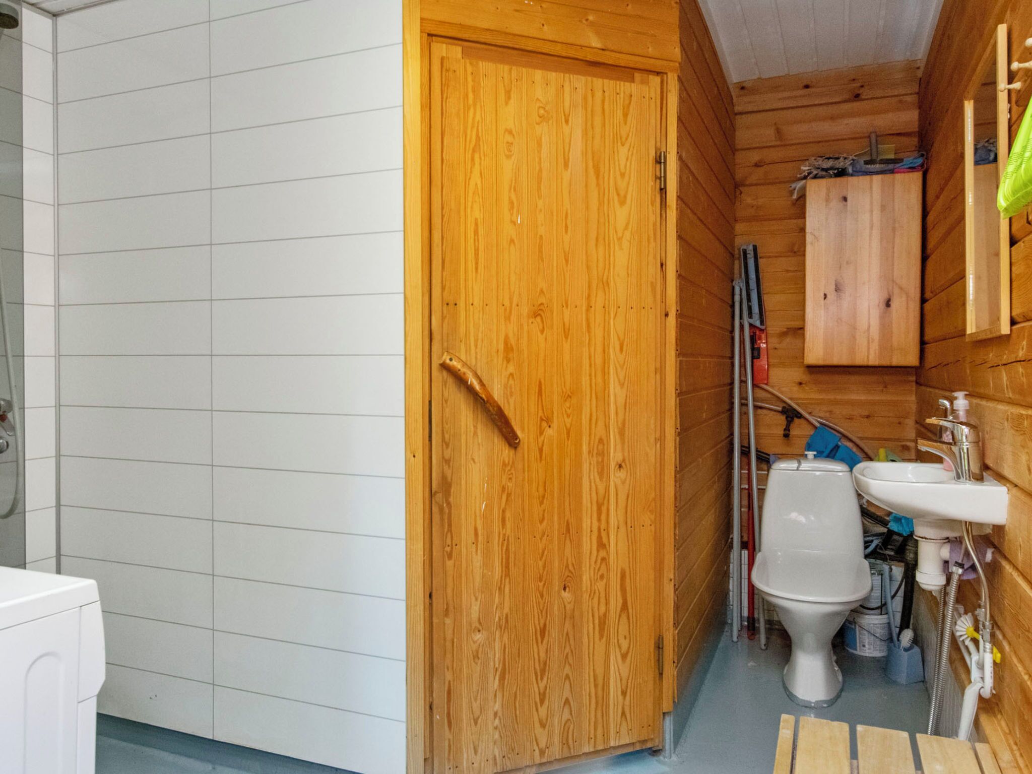 A compact wooden bathroom with a white toilet, a sink, and a shower area.