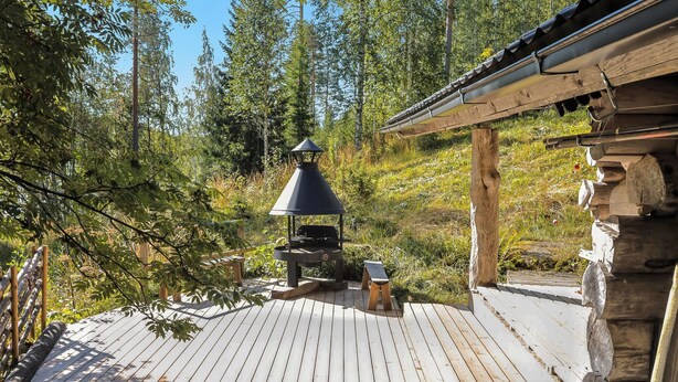 Eine Holzterrasse mit Grill und Sitzgelegenheit, umgeben von Bäumen.