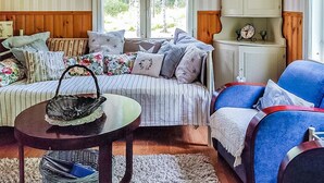 Un salon chaleureux avec un canapé à rayures, un fauteuil bleu, une table ronde en bois et un meuble contenant des objets décoratifs.