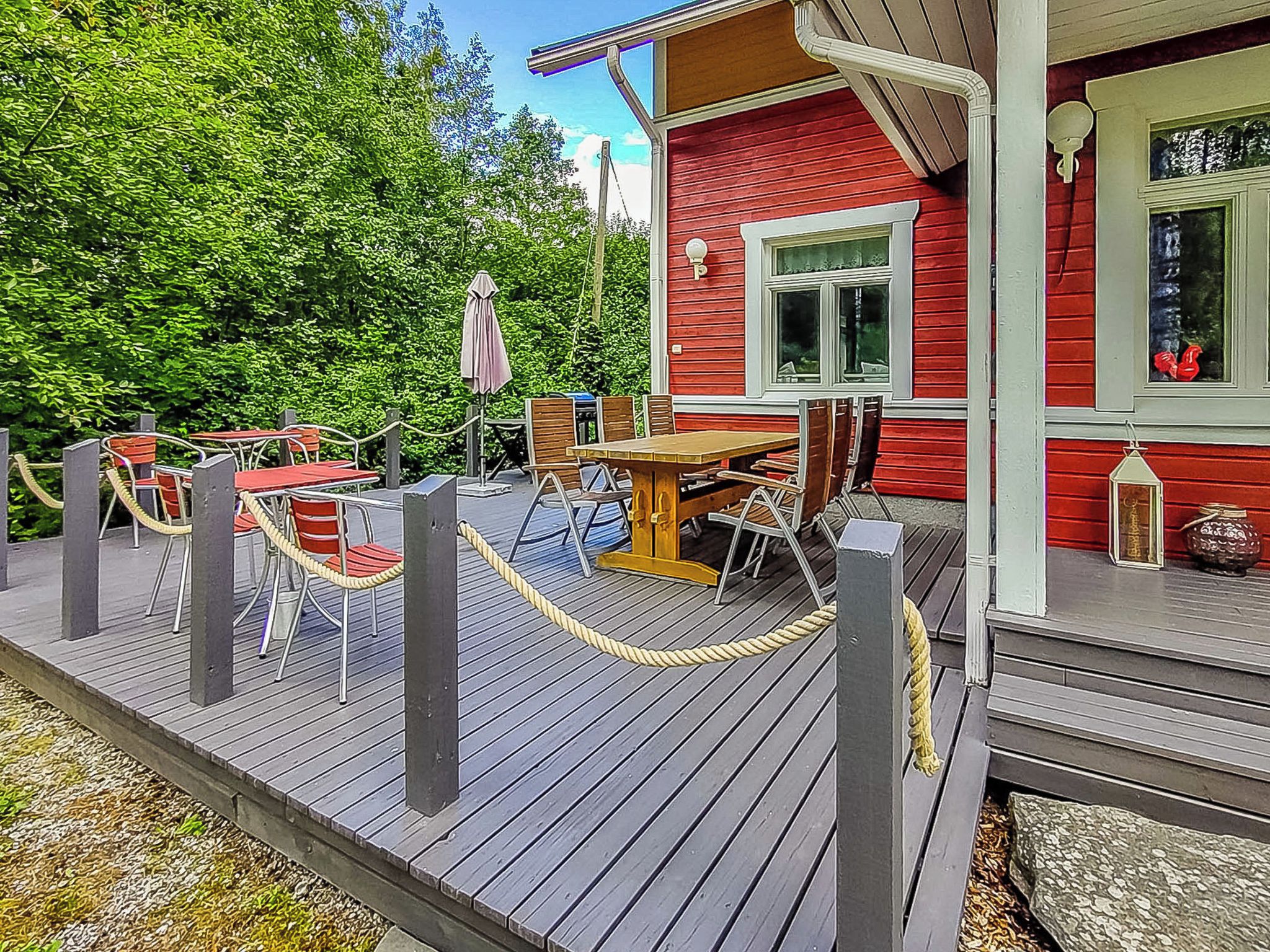 A wooden deck with outdoor seating, a red building with a window, and a rope barrier.