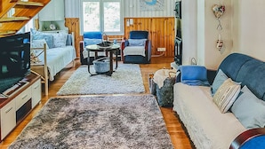 Un salon chaleureux avec un escalier en bois, un canapé, une télévision et un coin repas comprenant une table et des chaises.