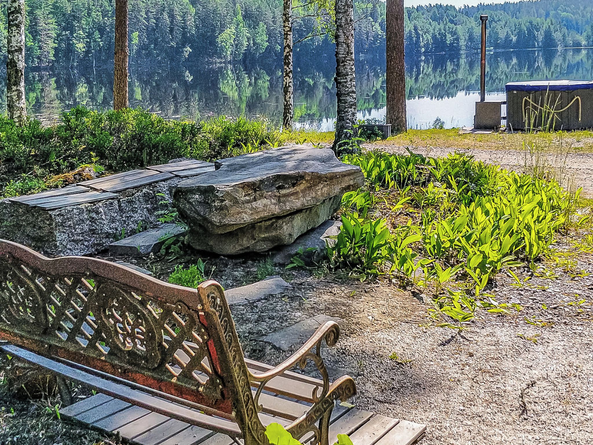 A wooden bench with intricate carvings, positioned on a gravel path with a stone wall and lush greenery.