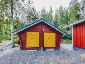 Eine rote Holzhütte mit zwei gelben Türen und einem blauen Dach, umgeben von Bäumen.