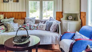 A cozy living room with a striped sofa, a blue armchair, a wooden cabinet, and a window with a view of trees.