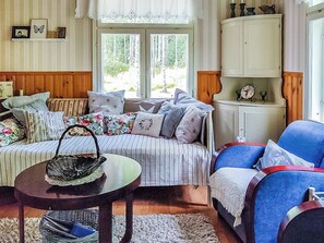 Ein gemütliches Wohnzimmer mit einem gestreiften Sofa, einem blauen Sessel, einem Holzschrank und einem Fenster mit Blick auf Bäume.