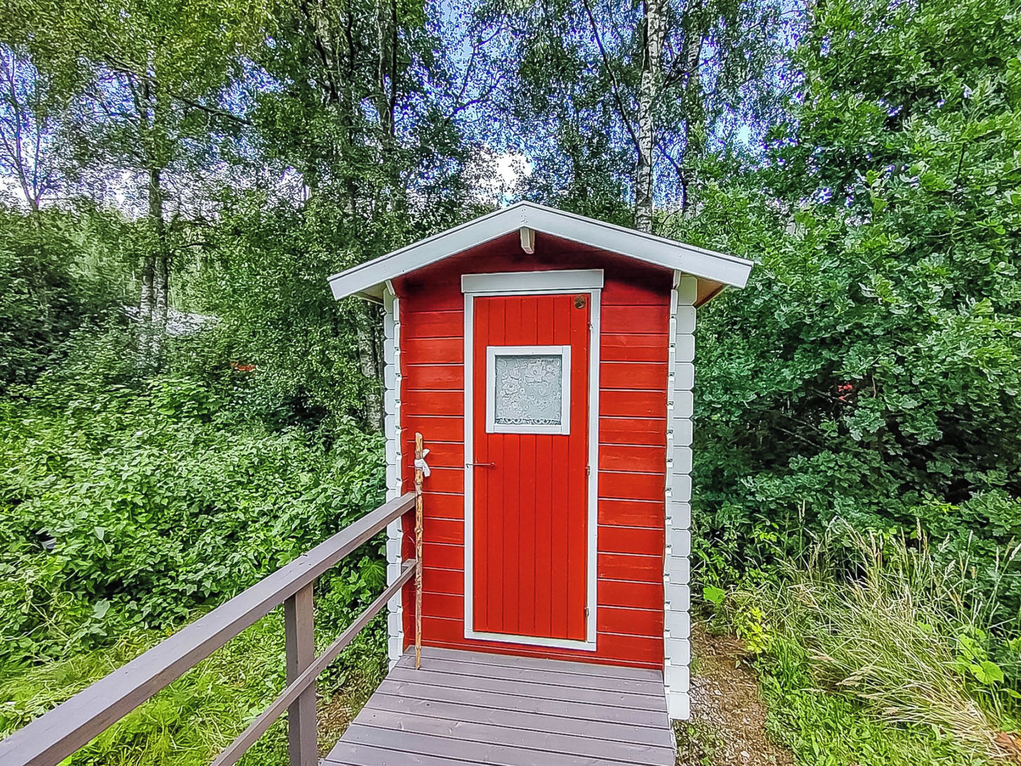 Eine rote Holzkonstruktion mit einer weißen Tür und einem kleinen Fenster, erreichbar über einen Holzsteg.