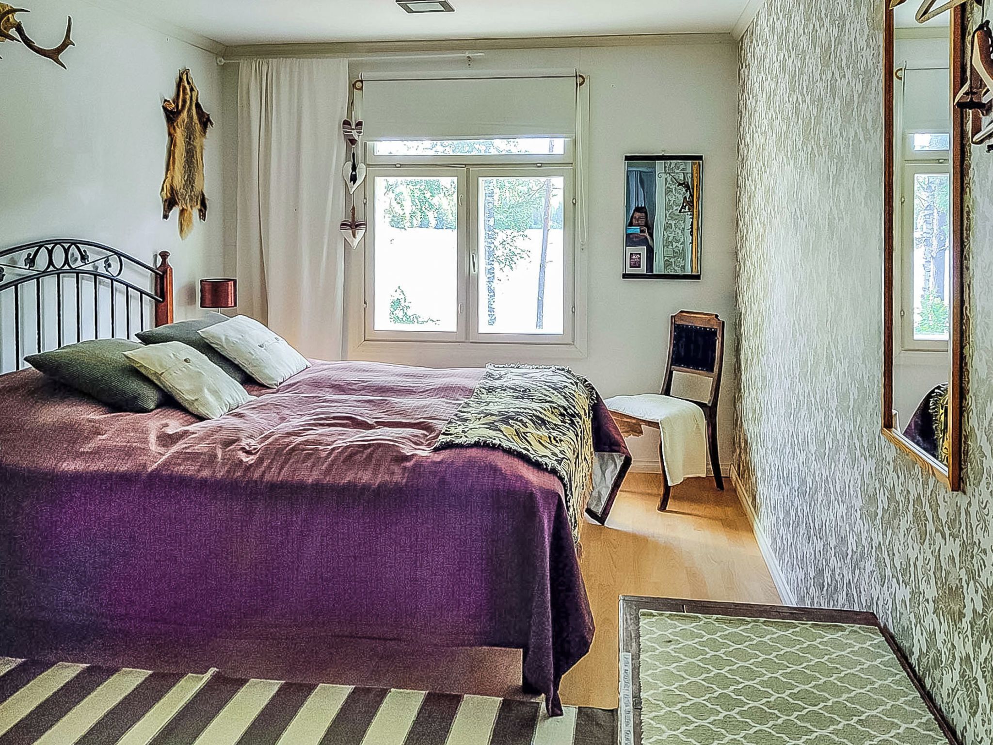 Een slaapkamer met een bed, een stoel, een raam en een spiegel.