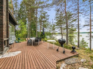 A wooden deck with outdoor furniture, a grill, and a view of a lake surrounded by trees. - Ranta-iivari by Interhome (Lohja)