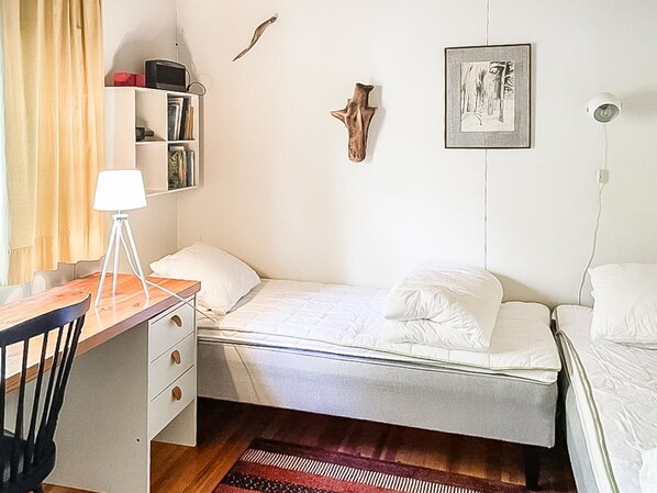 A bedroom with a bed, a desk with a lamp, a bookshelf, and a wall-mounted picture.