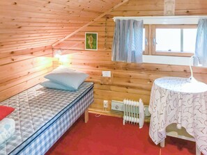 Pieni, viihtyisä huone, jonka seinät ovat puuta. Huoneessa on yksi sänky, jossa on ruudullinen patja, pieni pöytä kuviollisella pöytäliinalla ja patteri.