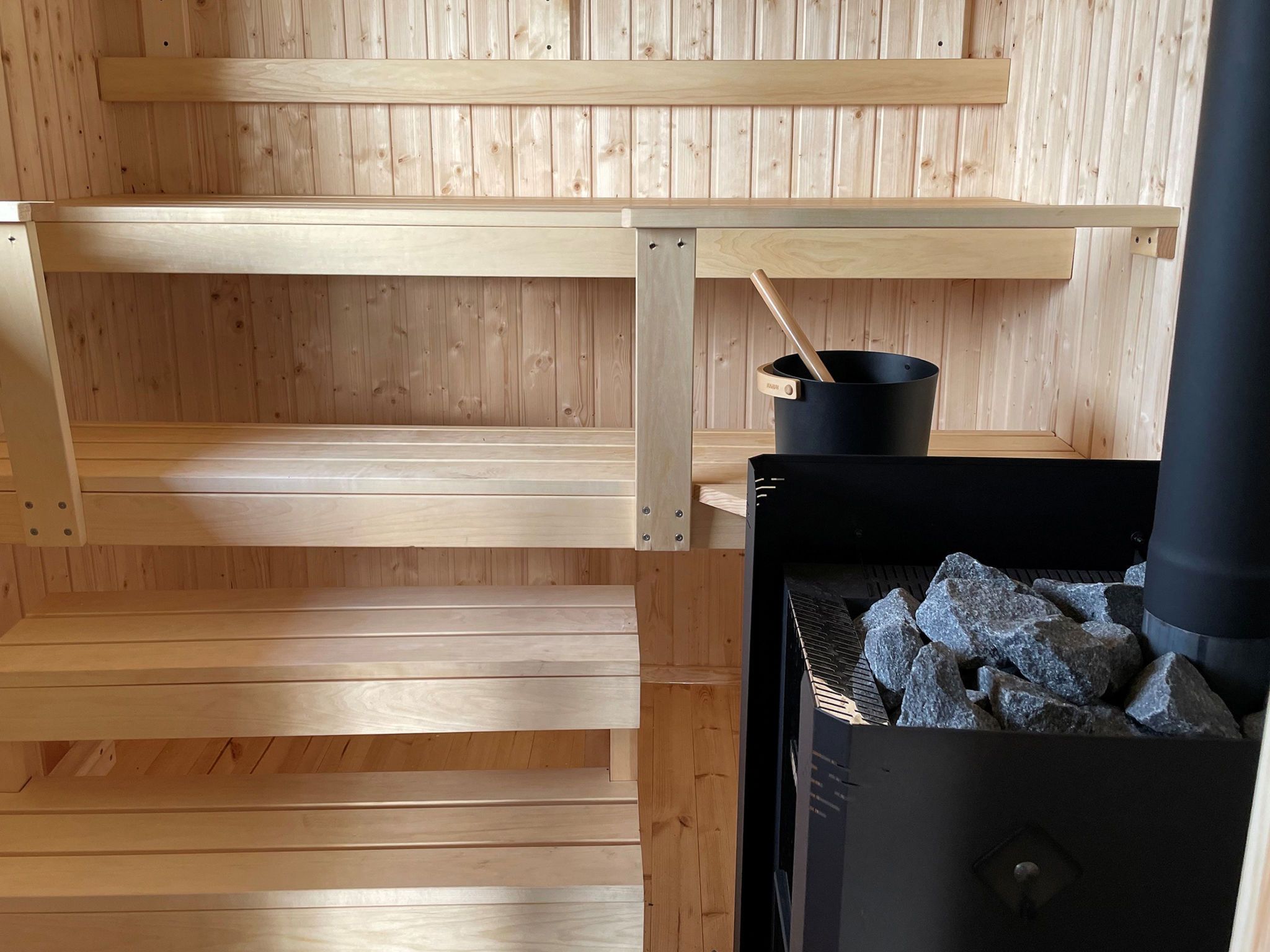 Een sauna met houten banken en een zwarte sauna-oven.