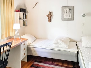 Un dormitorio con una cama individual, un escritorio con lámpara, una estantería y un cuadro colgado en la pared.