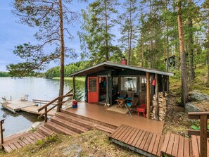 A cabin with a wooden deck, a small porch, and a dock extending into a lake.