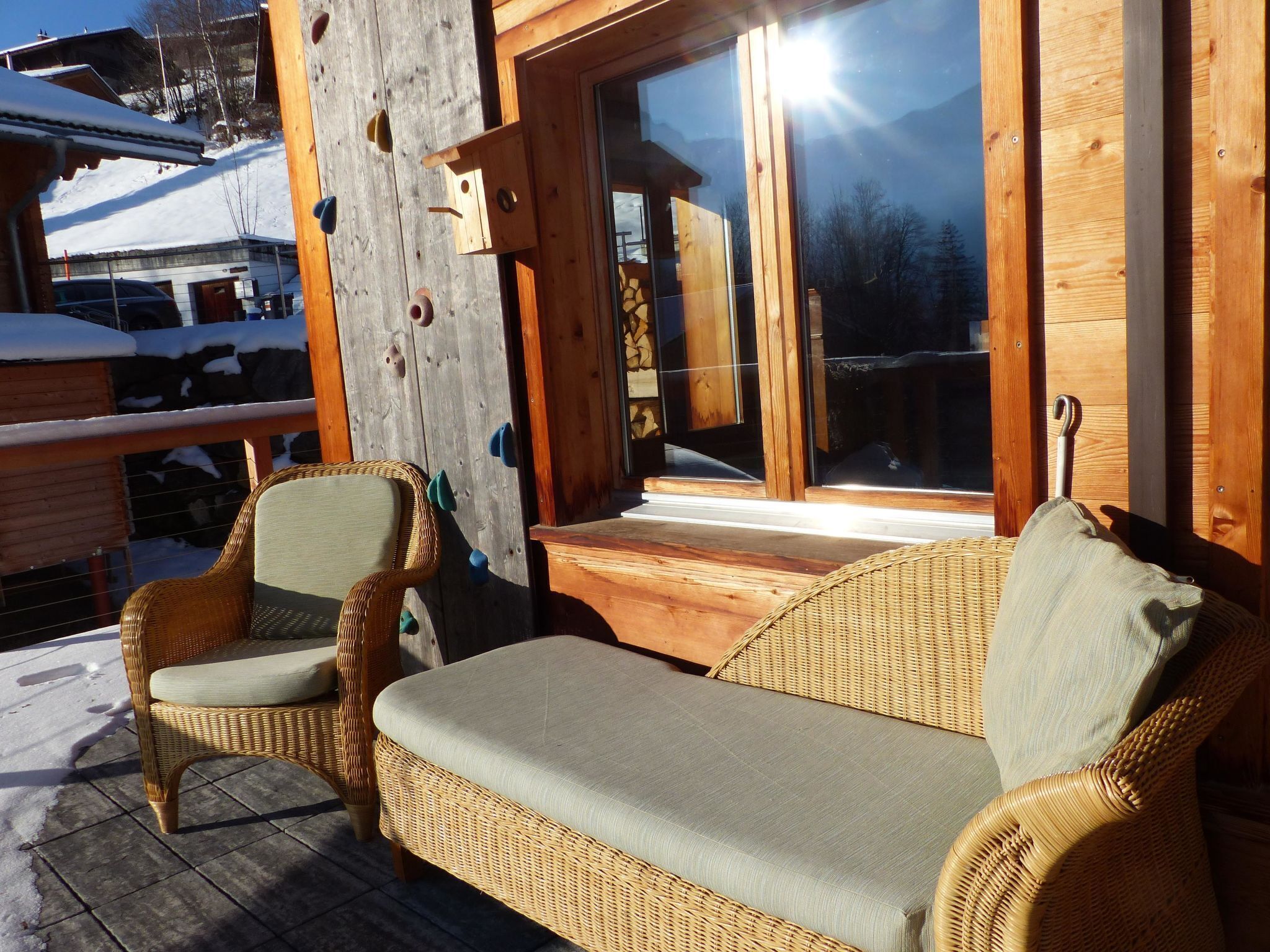 A wooden deck with wicker furniture, a glass door, and a snowy landscape in the background.