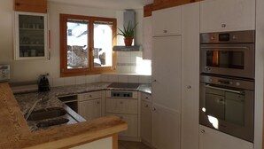 A kitchen with wooden cabinets, a built-in oven, and a window with a view of a snowy landscape. - Strubelblick EG by Interhome (Lenk)