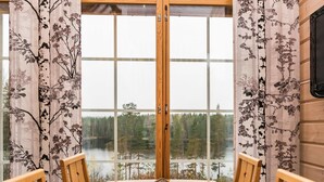 Een eetruimte met een tafel en stoelen, een uitzicht op een meer en bos door grote ramen, en een houten inrichting.