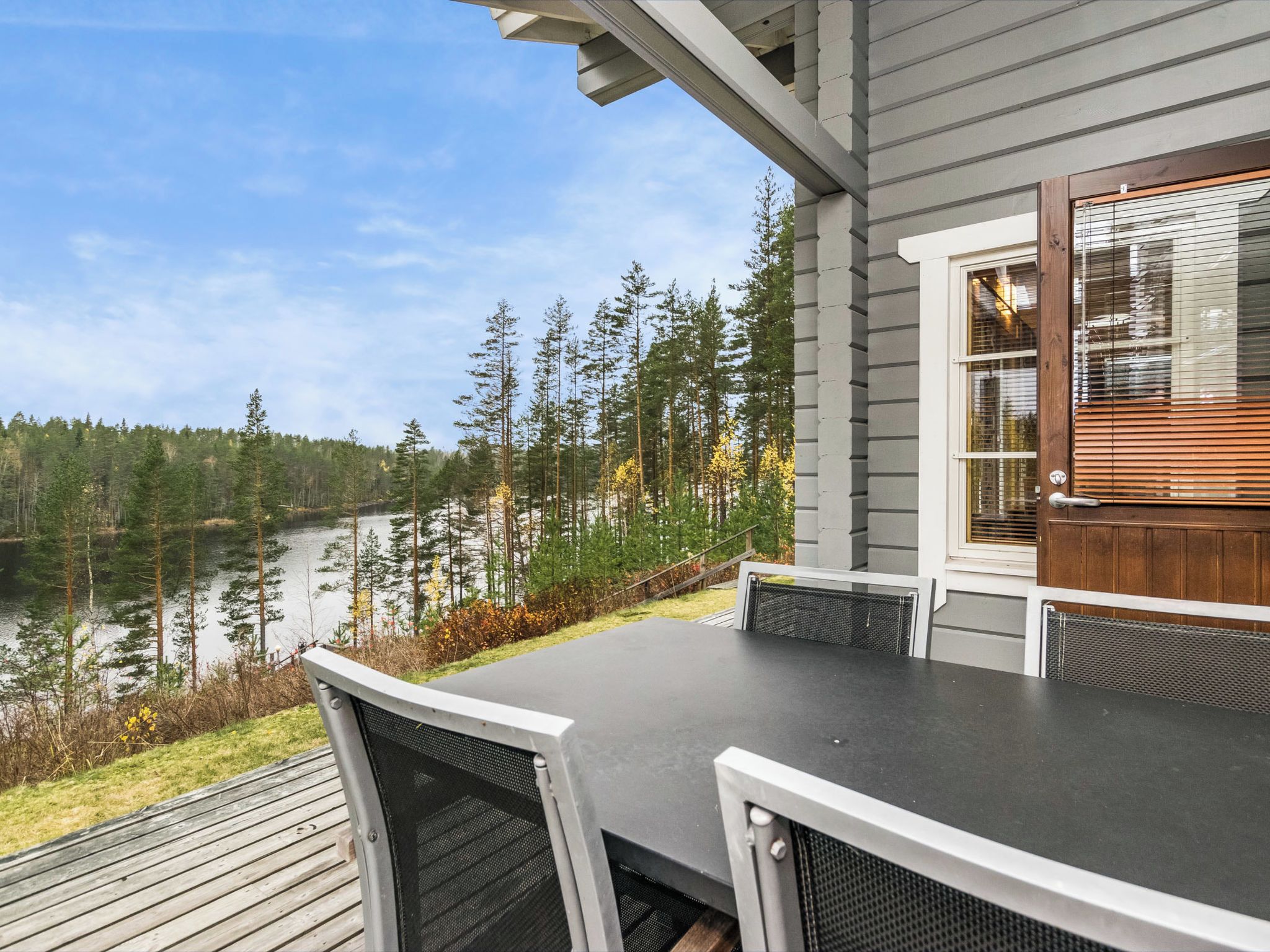 Une terrasse avec une table et des chaises donnant sur un lac, entourée d’arbres.