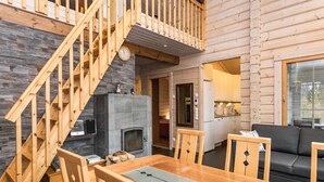 Een gezellig interieur van een chalet met een houten trap, een stenen open haard, een eethoek en een keuken.