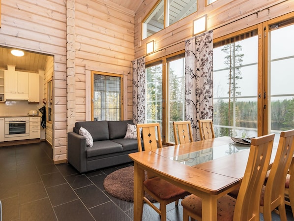 A wooden cabin interior with a dining table, chairs, a sofa, and a kitchen area.